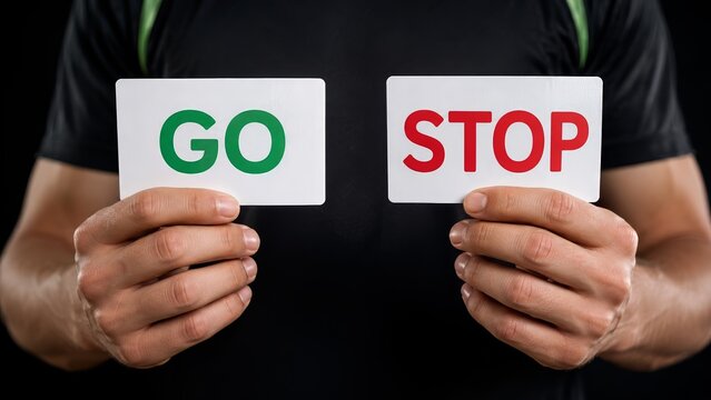 hands holding decision cards with green go and red stop text against black clothing, illustrating proceed or halt choice, permission, warning, traffic signal concept, decision making and control