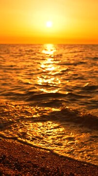 Sunset ocean beach waves gently washing onto the pebbled shore under a golden sun during a calm summer evening