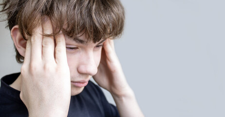 Fototapeta premium Young man suffering from a painful headache or migraine, holding his temples with both hands, conveying stress, mental fatigue, and a health problem