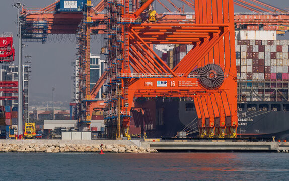 Mersin, Turkey - February 22, 2026: Massive orange Ship-to-Shore (STS) gantry cranes and container ship at the Mersin International Port (MIP).