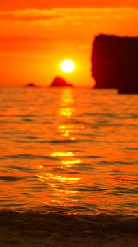 Ocean waves gentle motion flow towards rocky silhouette during golden dusk light at Mediterranean coastline. Vertical static close up shot.