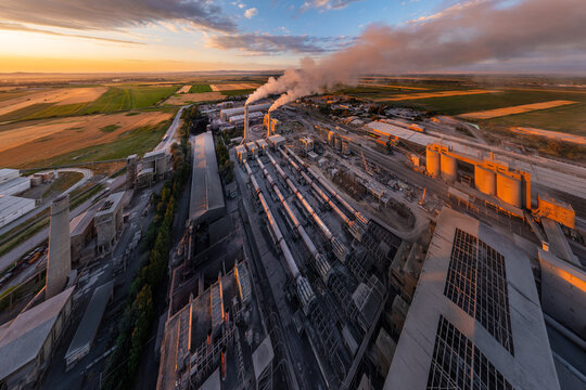 ultra-wide planar projection aerial view of Industrial cement plant with smokestacks and agricultural fields at sunset