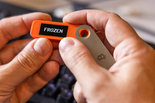 hardware Bitcoin wallet in a hands with message FROZEN on screen