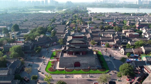 Aerial panorama of an ancient Chinese city featuring traditional multi-tiered architecture, adjacent water bodies, and modern urban skyline in the distance.