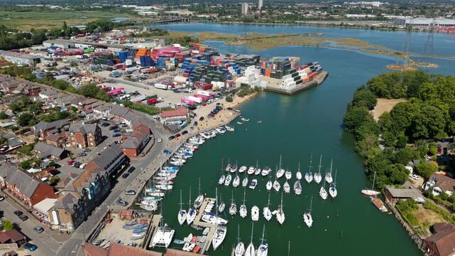 Aerial view of sailing yachts moored in Eling Creek beside a busy shipping terminal with stacked cargo containers in Southampton, Hampshire, UK