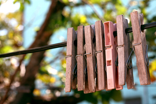Row of vintage wooden clothespins and one pink plastic peg on a clothesline outdoors
