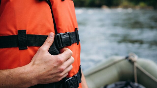 Man fastening orange life jacket strap with close man securing buckle near water vest buckle close with close