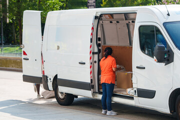 Delivery worker in an orange shirt unloading cardboard packages from a white cargo van © scharfsinn86