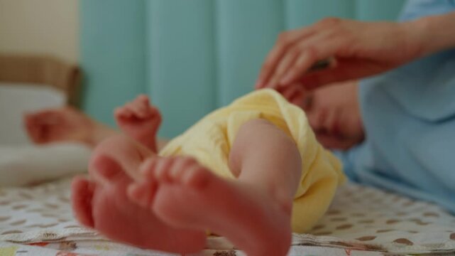 Close up of a newborn baby's tiny feet kicking and wiggling while lying on a changing mat, with a mother's gentle hands touching and playing with her infant in a tender moment