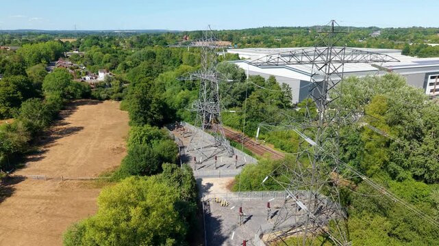 Aerial View of High Voltage Electricity Pylon with Train Passing on Railway in Background