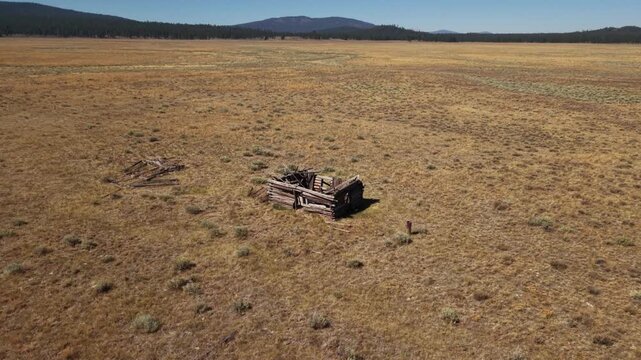 Drone ascends from ruined roofless cabin on remote Lassen County rangeland, revealing vast open landscape below.