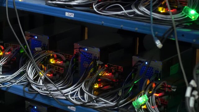 Oblique view of stacked hardware modules on blue shelving with bundled cables, glowing status lights, dense connectors, metallic surfaces, and layered industrial infrastructure