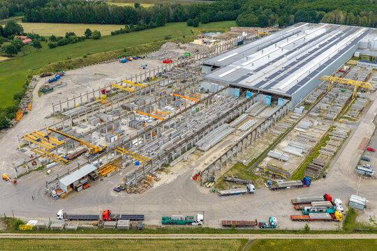 Aerial view of a prestressed concrete elements production yard with rows of precast beams, overhead gantry cranes, and transport trucks parked in the industrial facility in Poland.