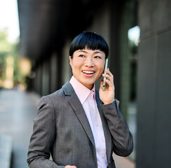 Portrait of a young asian japanese businesswoman woman using a smartphone mobile phone walking down...