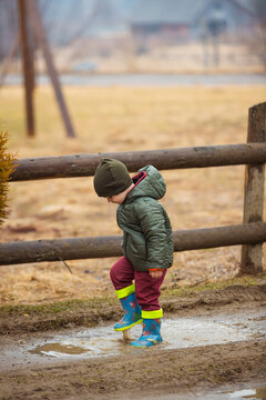 Little boy in protective rubber boots and rain clothes jumping in mud puddle. Happy child having fun while playing in puddle after rain.