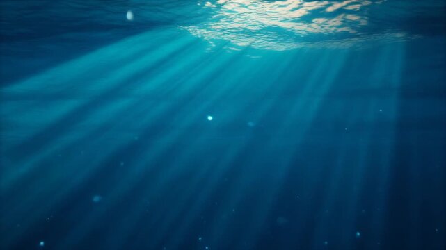 Underwater view of beautiful sun rays shining through the deep blue ocean water surface.