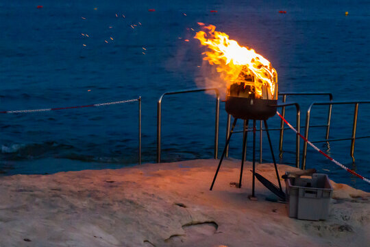 Flaming Portable Grill On Rocky Beach At Night With Ocean Background And Sparks