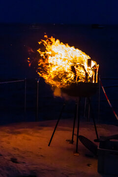 Flaming Portable Grill On Rocky Beach At Night With Ocean Background And Sparks