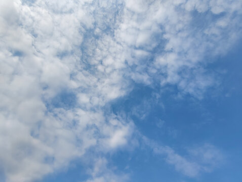 Blue sky with natural Altocumulus clouds scattered in a soft, dappled pattern. Daytime meteorology background.
