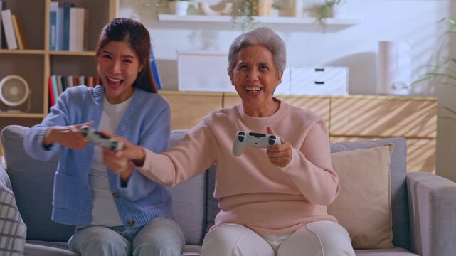 Granddaughter grandmother game controller sofa living room smiling senior woman family bonding leisure activity video game together cozy home joyful pair happy expression
