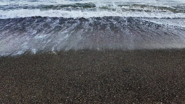 POV tilt down to the sand and back up to ocean waves on a beach in Ireland in winter