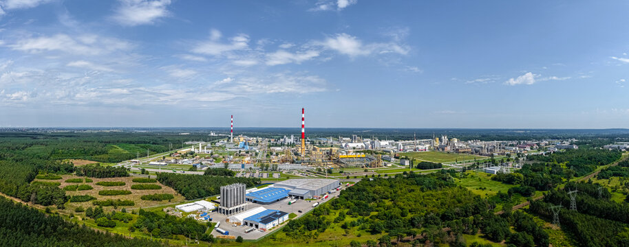 Wloclawek, Poland - 10 August 2026: Aerial view of the ORLEN PTA plant, featuring industrial infrastructure, tall chimneys, and surrounding green forests under a blue sky.