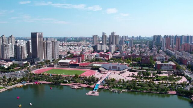 Aerial view of an urban area featuring a stadium, lake, high-rise buildings and green spaces under a clear blue sky.