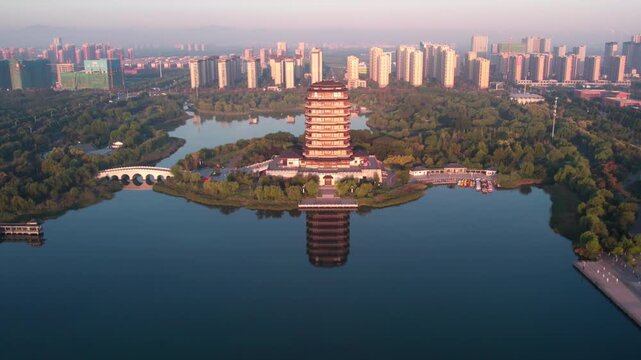 An aerial view of a traditional pagoda standing on an island in a park lake, with urban high-rises in the background.