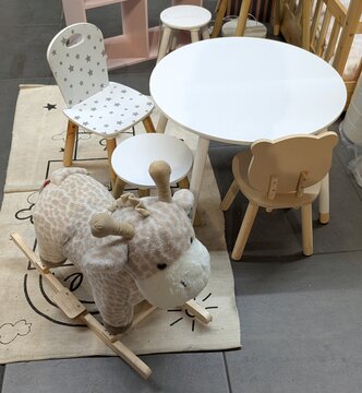 Rinc&oacute;n de juego infantil, con una mesa con sillas y taburetes, un balanc&iacute;n de peluche con forma de jirafa y una alfombra 