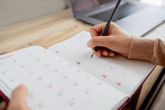 Close-up of a woman's hand writing in a lined notebook, planning appointments, tasks, schedules and daily activities.