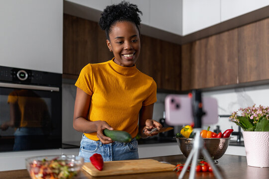 Woman cooking with vegetables in kitchen while recording a video on smartphone
