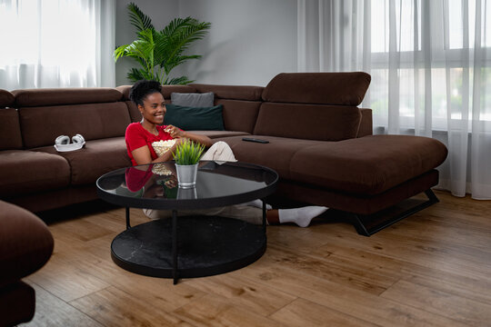 Young woman sitting on sofa in living room, enjoying a snack while watching TV