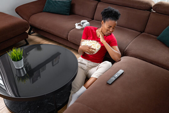 Woman sits on sofa holding popcorn while watching TV in living room during evening time
