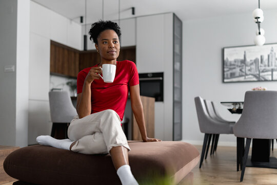 Woman sitting on a couch holding a white cup in a modern living room with gray and wooden decor