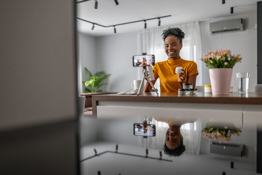 Woman smiling while recording a video in a modern kitchen with plants and flowers