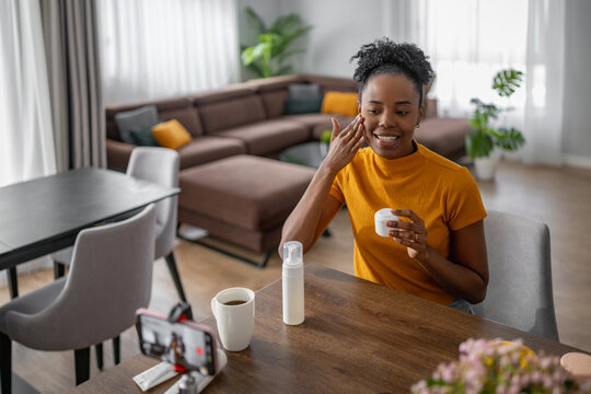 Woman applies moisturizer while sitting at dining table in modern living room during the morning