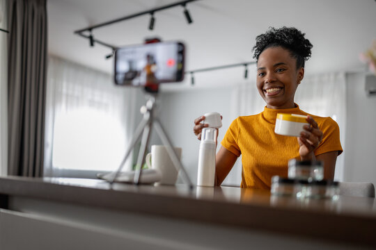 Woman making a video while holding a cup and a bottle in a home setting