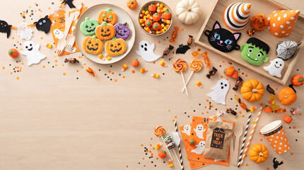 Fototapeta premium Creative Halloween flat lay background with festive cookies, candies, cute decorations, and small pumpkins on a wooden table