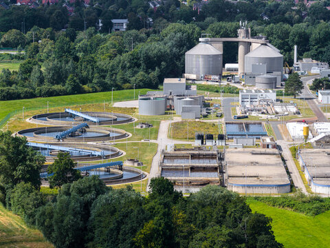 Cuxhaven, Germany - 11 August 2026: Aerial view of a wastewater treatment plant with circular sedimentation tanks, filtration basins, and industrial silos surrounded by green fields.