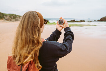 Rear view of backpacker holding compass against  backdrop of ocean. Female hiker looks at compass or direction outdoors. Concept of adventure, navigation, and hiking. © Koval988