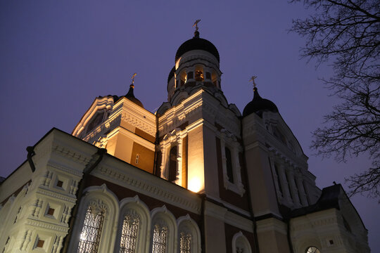 Low-angle view of the illuminated Alexander Nevsky Cathedral with onion domes and ornate exterior details against dusk sky in Tallinn