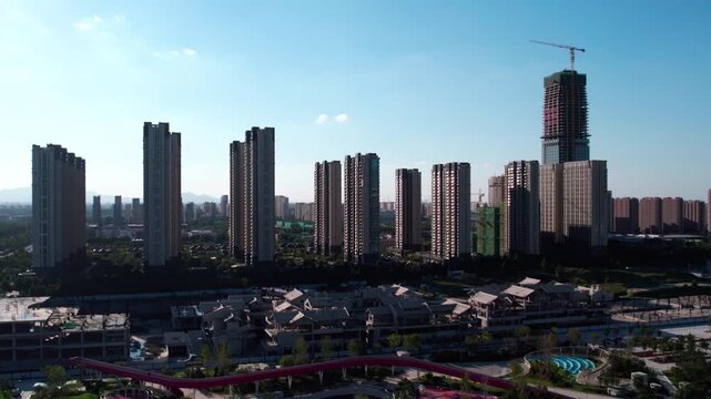 A daytime urban landscape featuring high-rise residential buildings, a skyscraper under construction, and green spaces in the foreground.