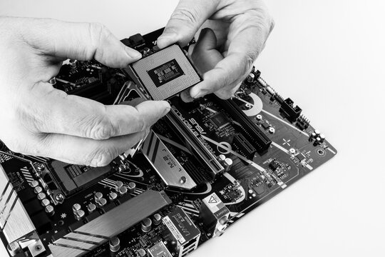 Maykop, Russia - February 18, 2025: men's hands hold the new Intel processor above the Asus motherboard close up, black and white photo