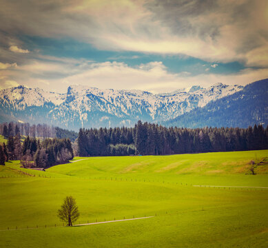 Scene featuring vintage retro hipster style travel view of German idyllic pastoral countryside in spring with Alps in background. Bavaria, Germany