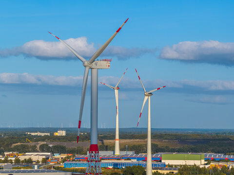 Bremen, Germany - 12 August 2026: Aerial view of wind turbines at Bremerhaven Harbor with industrial buildings and warehouses in the background under a blue sky.