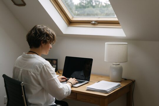 Woman working remotely as a freelancer at a wooden desk with natural light from a skylight.