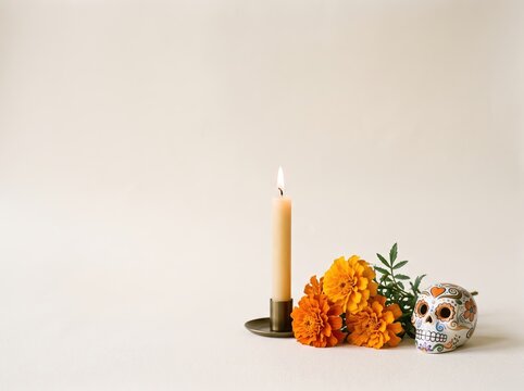 Minimal altarpiece arrangement with lit candle, marigold flowers and sugar skull for dia de muertos background and banner design