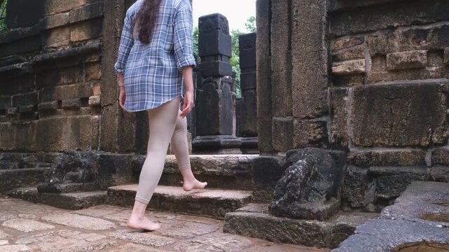 Barefoot woman walking up stone stairs entering ancient Nalanda Gedige temple in Sri Lanka