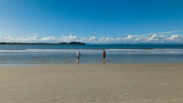 Paranagua, State of Parana, Brazil - 05 February 2026: Aerial view of Ilha do Mel with two people walking in the shallow water along the sandy coastline under a clear blue sky.