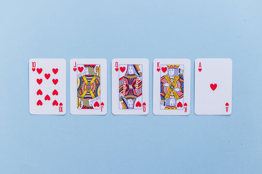Royal flush hand of hearts playing cards arranged in a row on a light blue background. Minimalist flat lay top view stock photo representing luck, success, winning, and poker strategy.